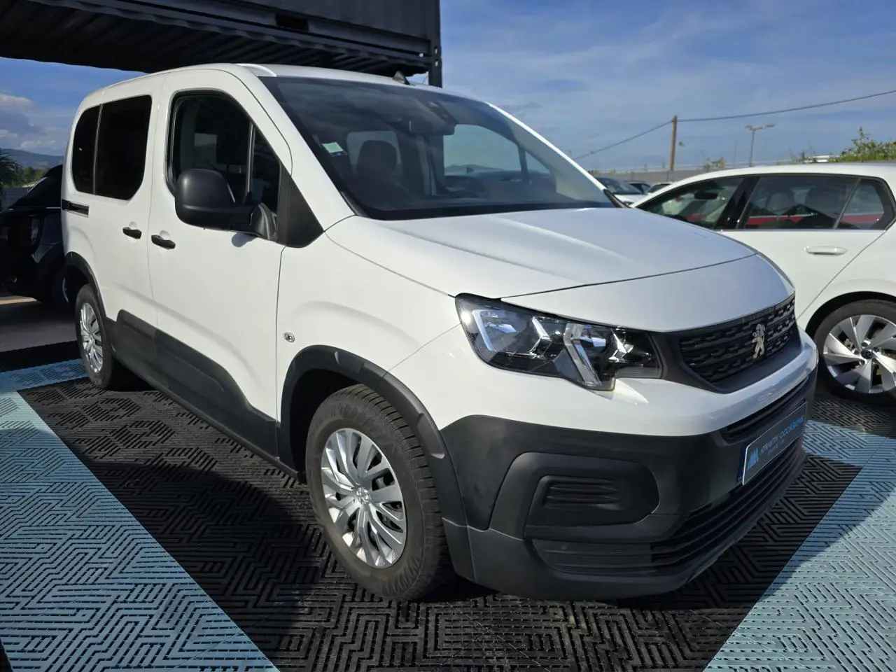 Peugeot Rifter blanc banquise en 3/4 avant droit, avec protections noires sur pare-chocs et bas de caisse.