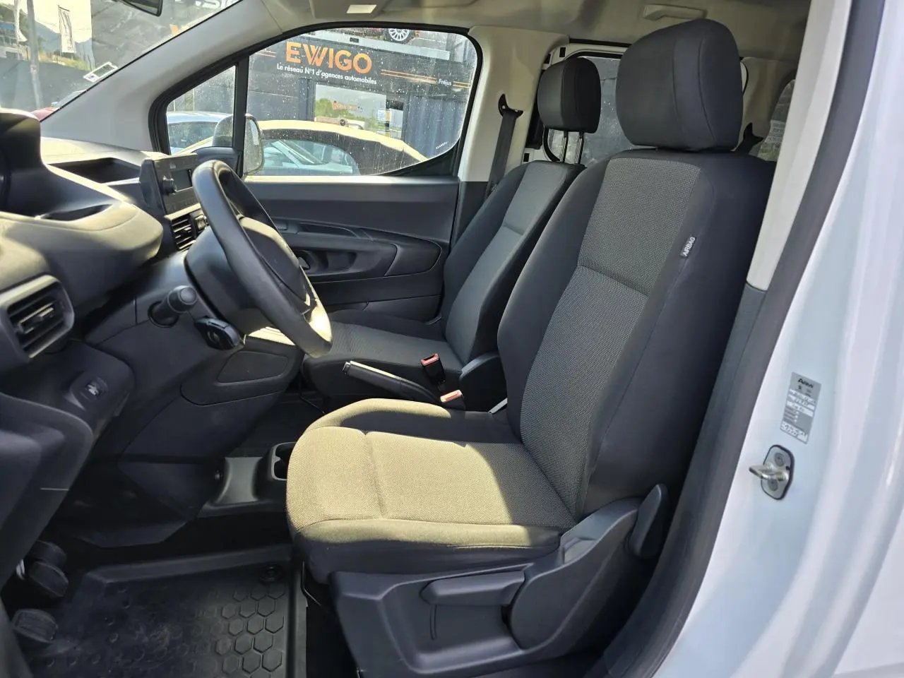 Vue intérieure côté conducteur du Peugeot Rifter blanc Banquise 2021, sièges tissu gris et tableau de bord noir.