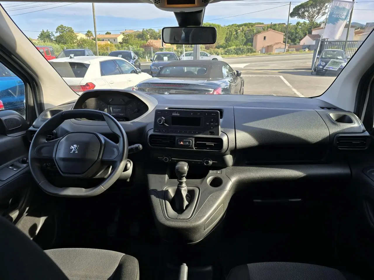 Vue intérieure avant du Peugeot Rifter 1.5 BlueHDi blanc, montrant le volant, tableau de bord et levier de vitesses manuel.