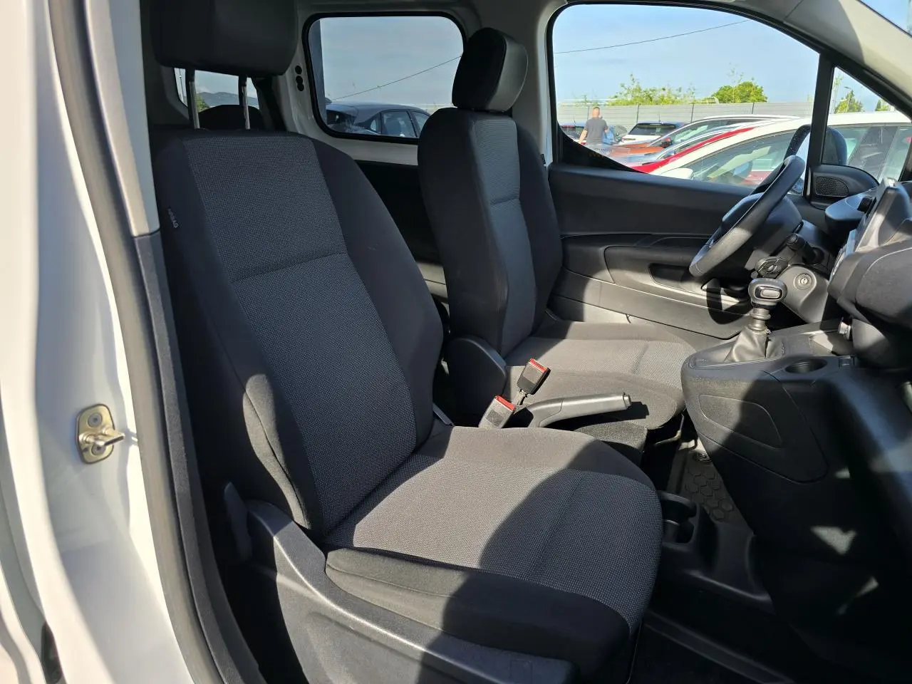 Vue intérieure côté conducteur du Peugeot Rifter 1.5 BlueHDi 100, montrant les sièges tissu gris et la boîte manuelle.