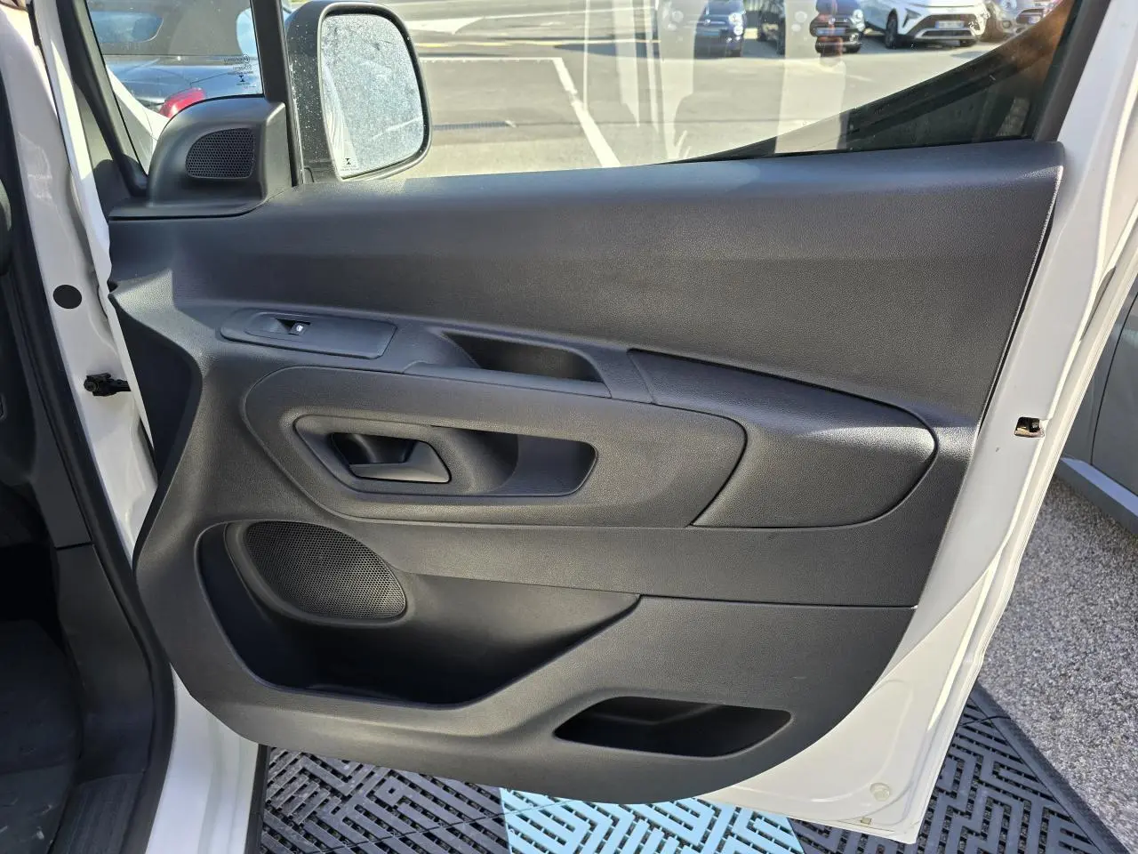 Vue de la porte avant gauche ouverte d’un Peugeot Rifter blanc banquise, avec panneau intérieur noir et commande de lève-vitre.