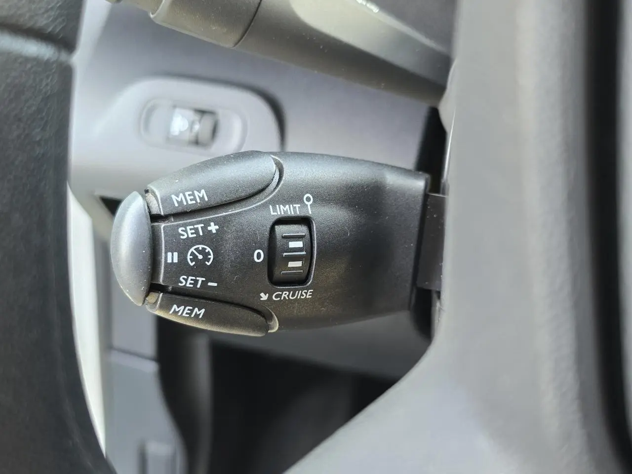 Gros plan sur la commande de régulateur de vitesse noire à gauche du volant du Peugeot Rifter blanc banquise 2021.