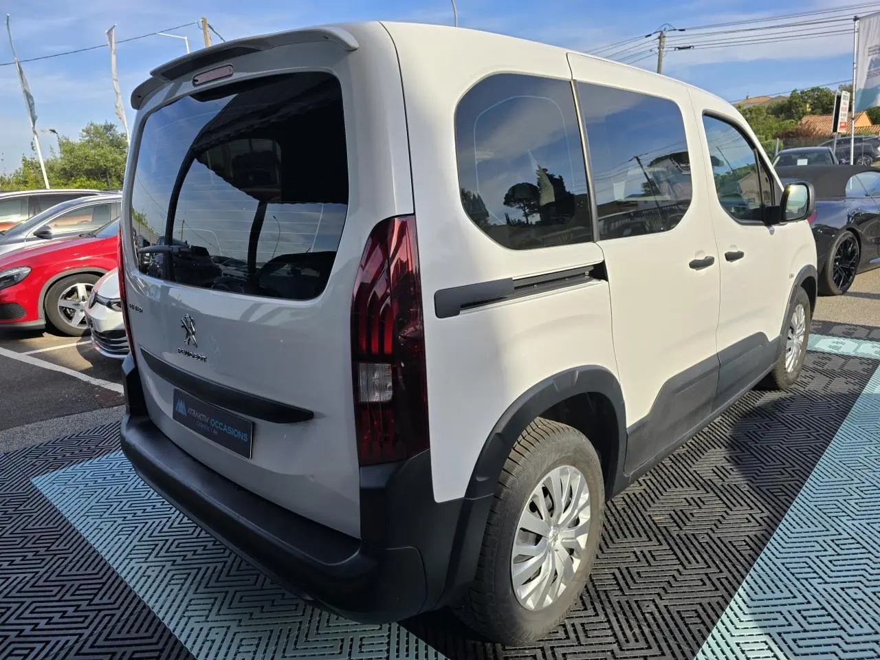 Vue 3/4 arrière droite du Peugeot Rifter blanc Banquise avec vitres teintées et protections noires sur pare-chocs et bas de caisse.