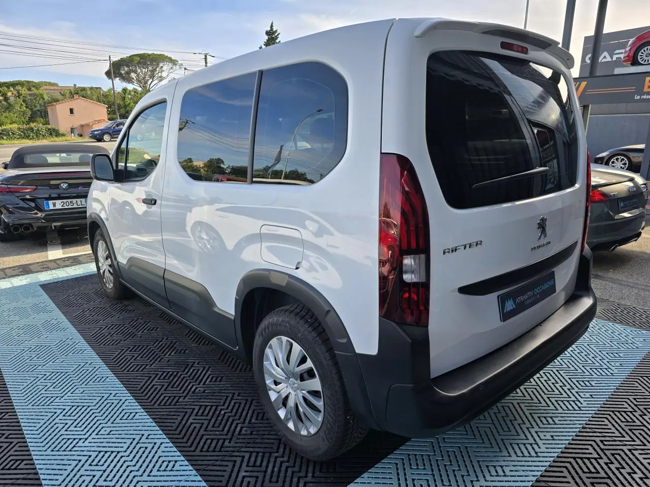 Vue 3/4 arrière droite d'un Peugeot Rifter blanc banquise avec vitres teintées et jantes tôle 16 pouces.