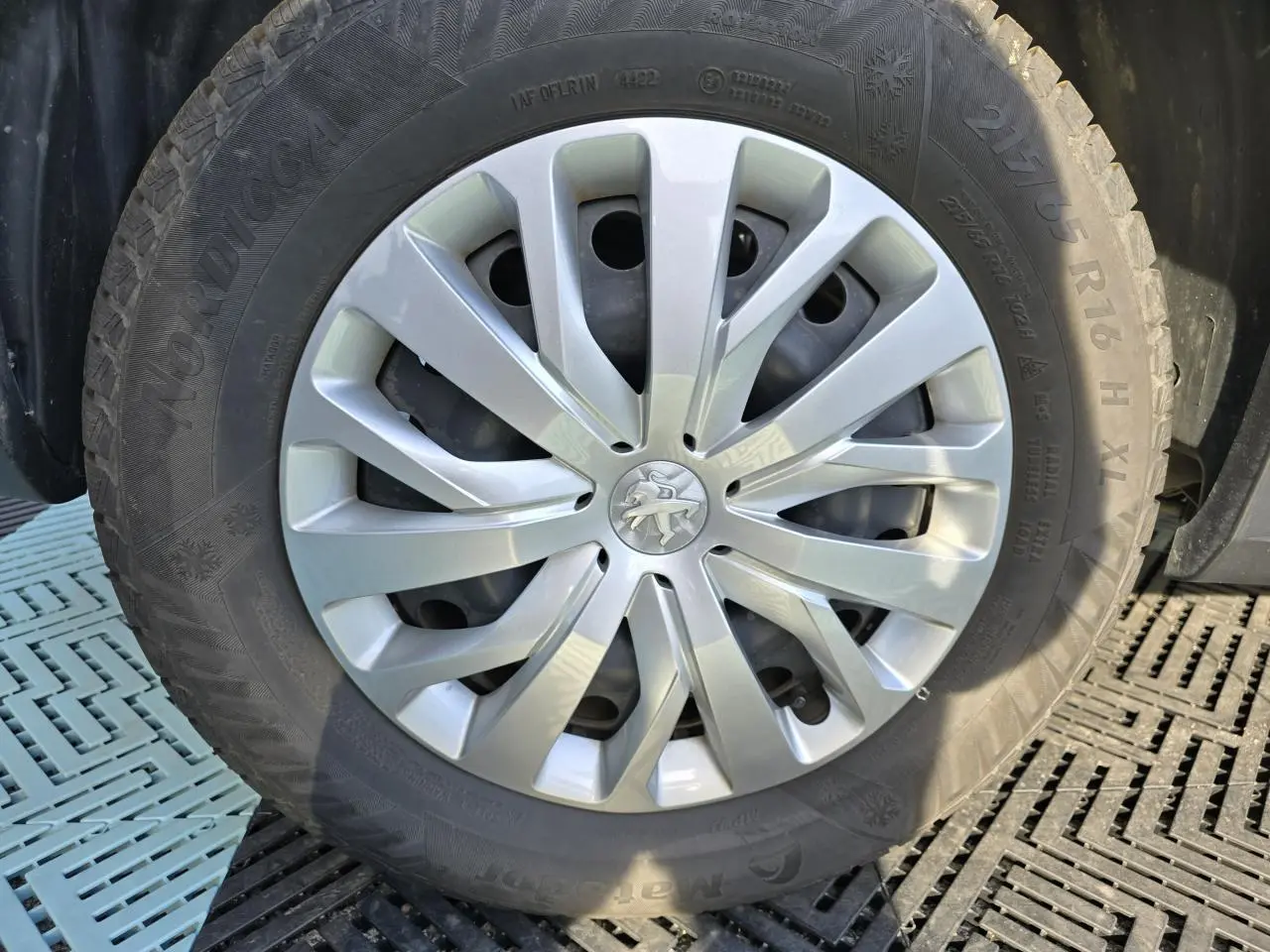 Gros plan sur la roue avant droite du Peugeot Rifter blanc Banquise avec enjoliveur argenté et logo lion central.