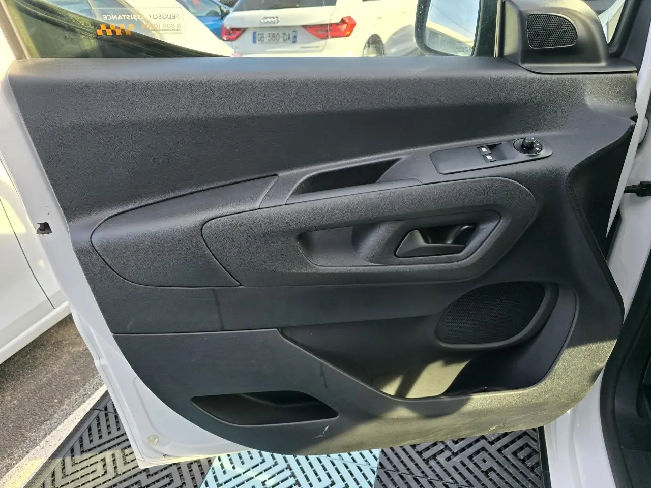 Vue intérieure de la porte avant gauche noire du Peugeot Rifter blanc Banquise 2021 avec commandes électriques et haut-parleur intégré.