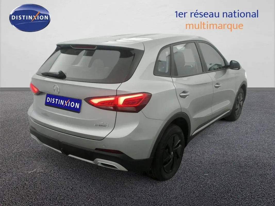 Vue 3/4 arrière droite du SUV MG ZS 1.5 L Hybrid+ 2026 en Cosmic Silver avec feux arrière allumés.