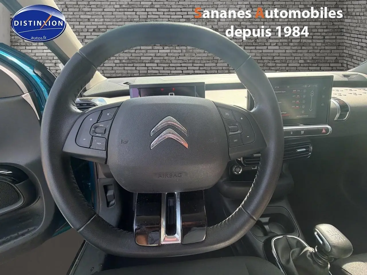 Vue intérieure centrée sur le volant cuir de la Citroën C4 Cactus bleu métal, avec tableau de bord et levier de vitesses manuel visibles.