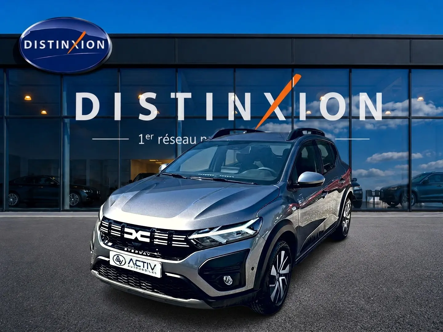 Dacia Sandero Stepway gris schiste vue 3/4 avant droit, avec barres de toit et jantes distinctives.