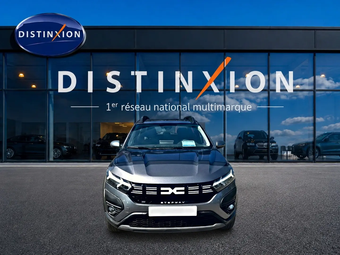 Vue avant d'une Dacia Sandero Stepway gris schiste avec calandre noire et barres de toit devant un showroom Distinxion.