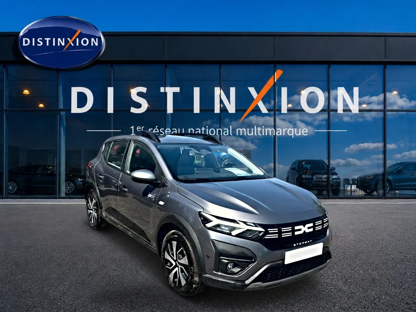 Dacia Sandero Stepway gris schiste vue 3/4 avant droit avec barres de toit et jantes distinctives.