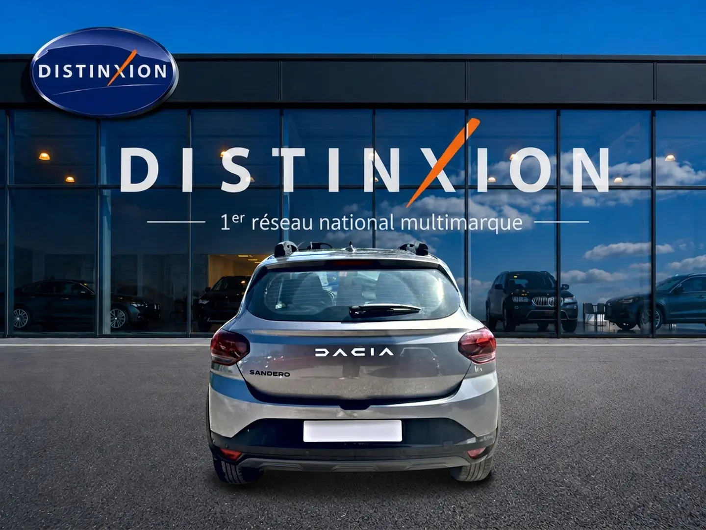 Vue arrière d'une Dacia Sandero gris schiste garée devant une vitrine avec logo Distinxion.