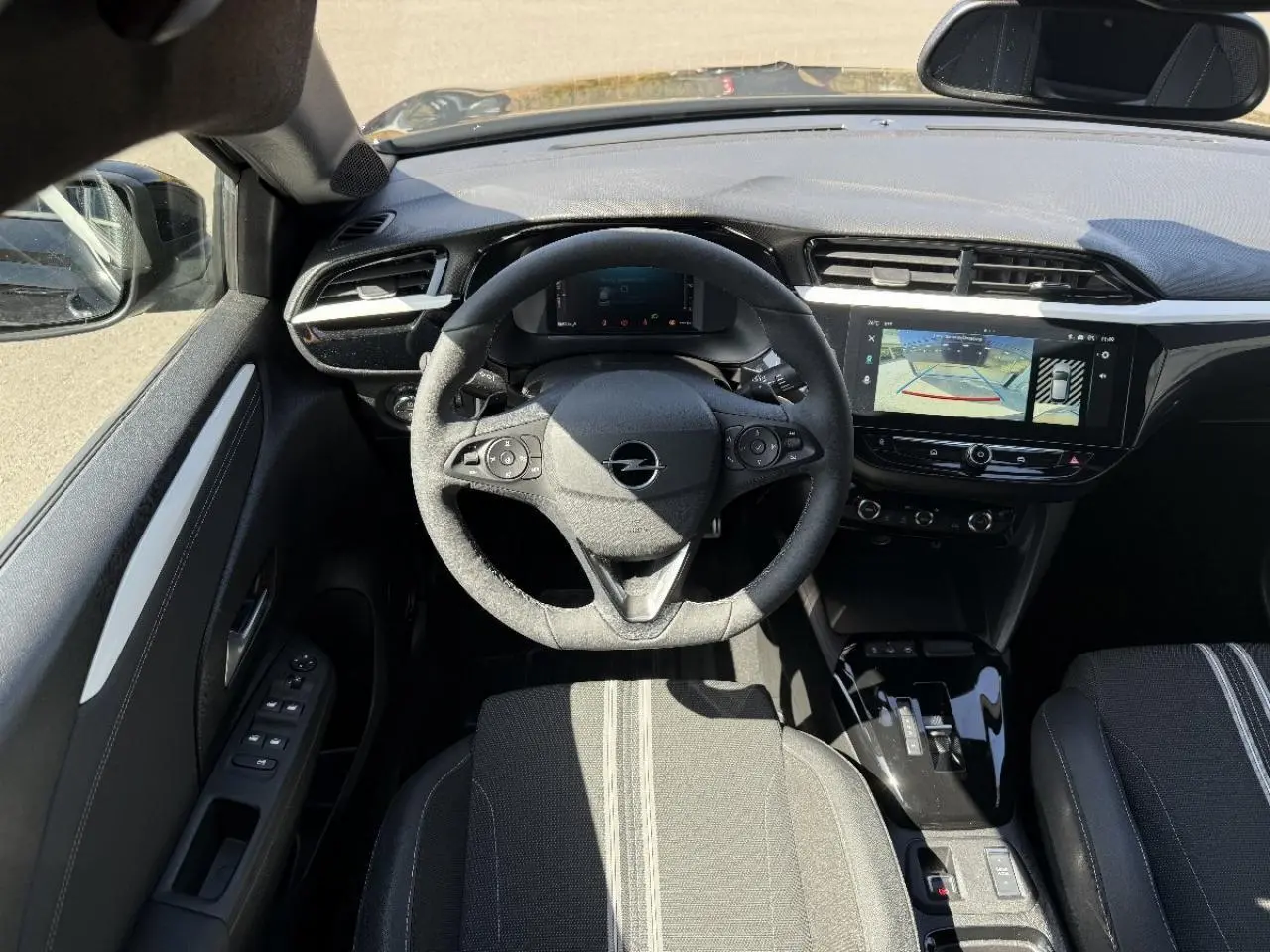 Vue intérieure centrée sur le volant et tableau de bord de l’Opel Corsa noir perla nera avec écran tactile et caméra de recul.