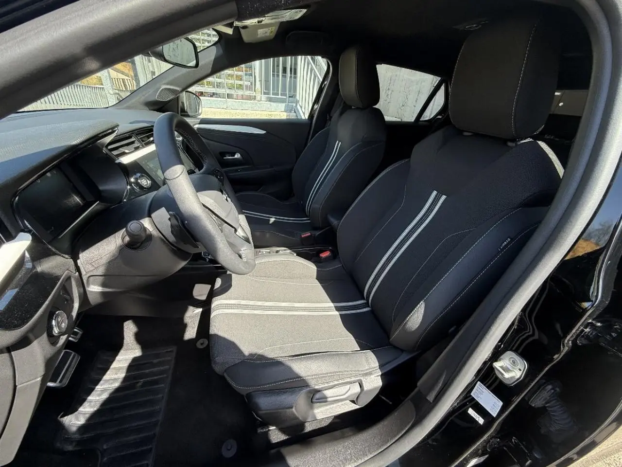 Vue intérieure côté conducteur de l’Opel Corsa 1,2 Hybrid 2025 noir perla nera, sièges tissu avec bandes blanches centrales.