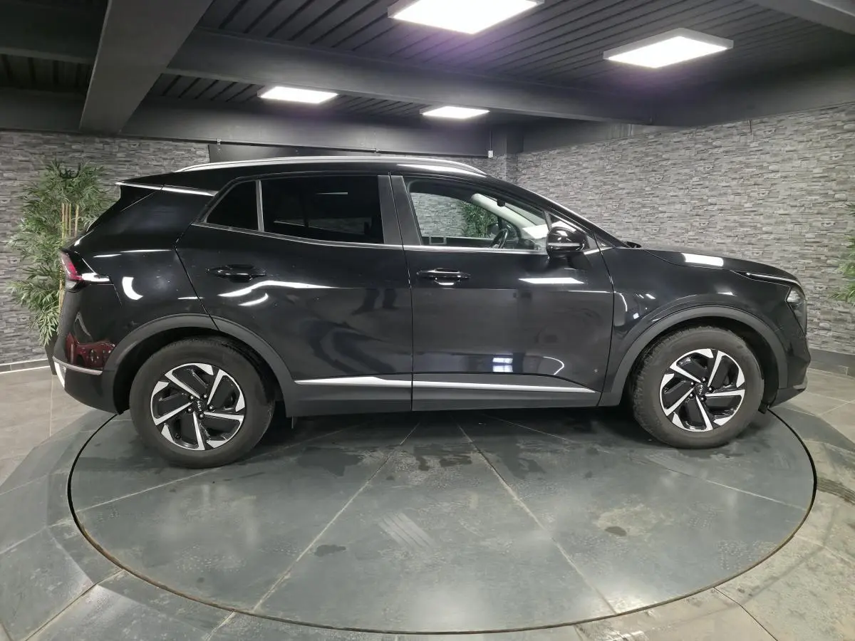 Profil côté gauche du SUV KIA SPORTAGE noir 2022 avec jantes alliage et vitres teintées dans un showroom.