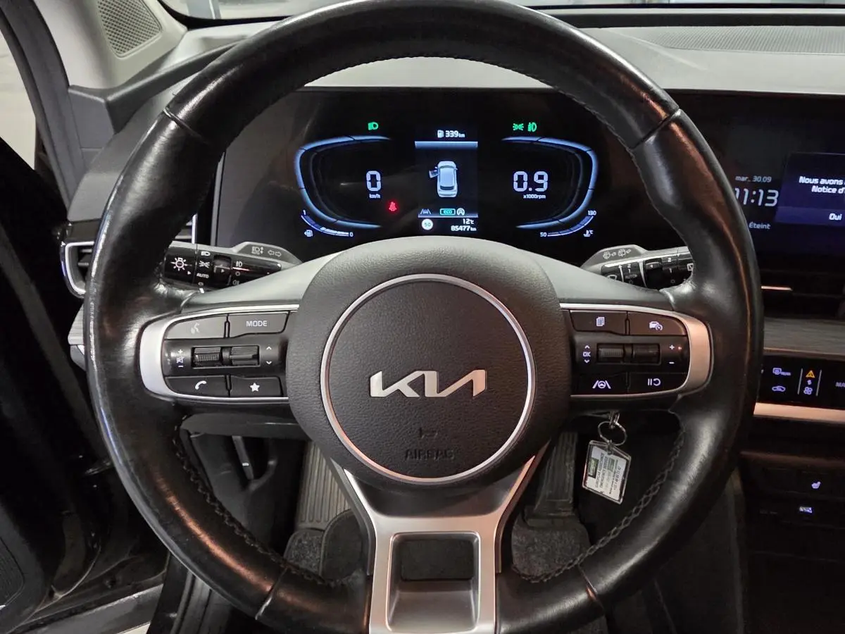 Vue rapprochée du volant cuir noir du Kia Sportage 2022 avec tableau de bord numérique allumé en arrière-plan.