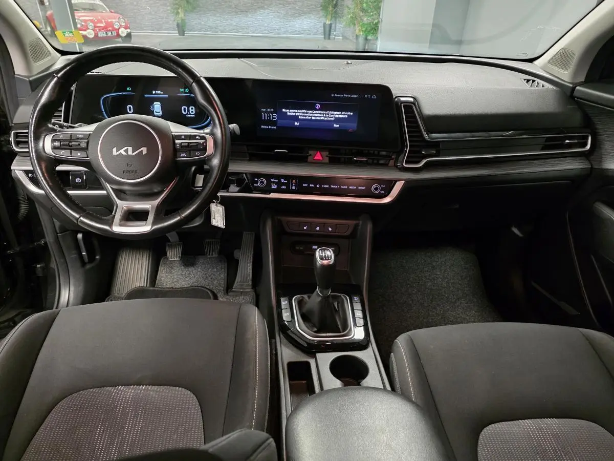 Intérieur noir du Kia Sportage 2022 vu de face, volant cuir, tableau de bord numérique et levier de vitesse manuel.