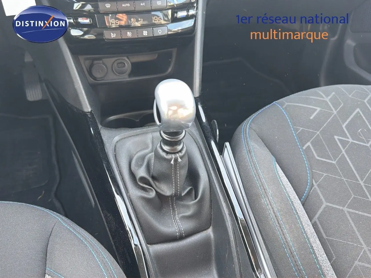 Gros plan sur la console centrale et levier de vitesse manuel d'une Peugeot 2008 gris platinium, sièges tissu noir avec surpiqûres bleues.