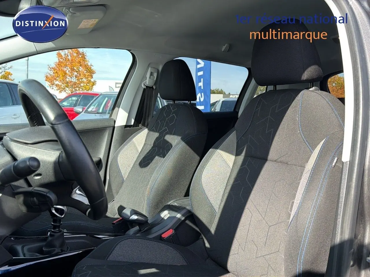 Intérieur du Peugeot 2008 gris platinium, vue côté gauche montrant les sièges avant en tissu noir avec surpiqûres bleues.