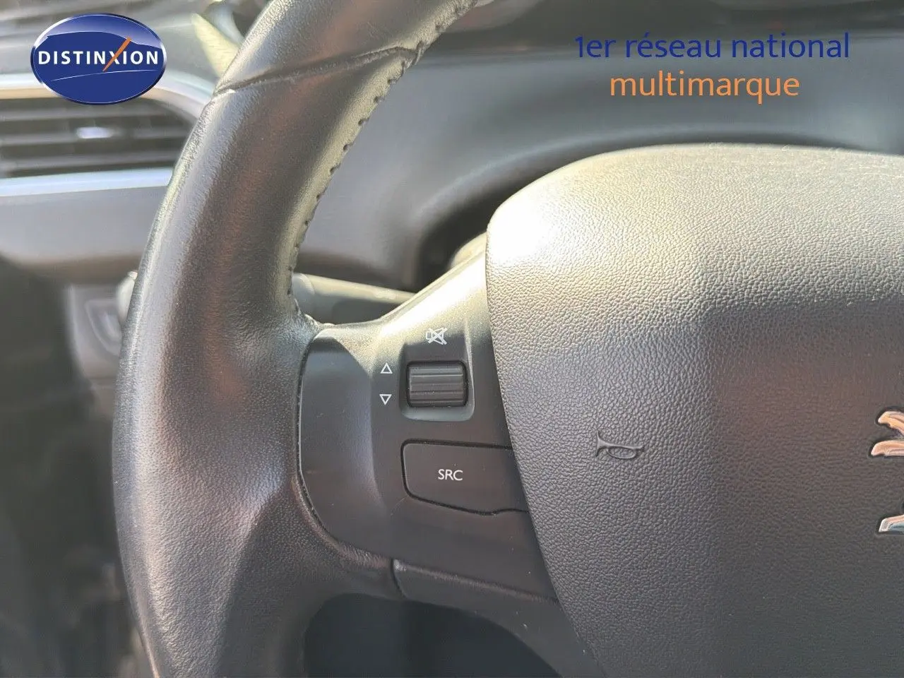 Gros plan sur le volant en cuir noir du Peugeot 2008 gris platinium, montrant les commandes audio intégrées.