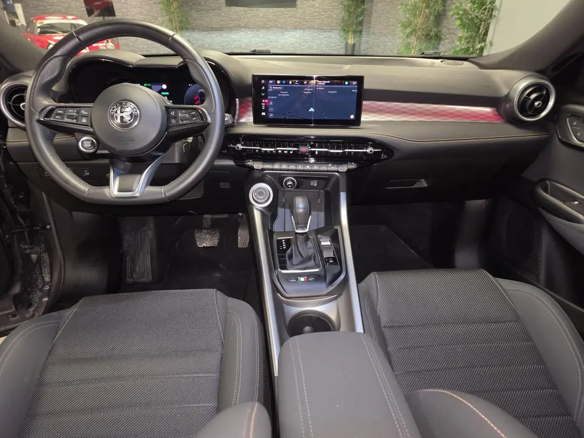 Vue intérieure avant de l'Alfa Romeo Tonale 2023, tableau de bord noir avec écran tactile et volant sport cuir.