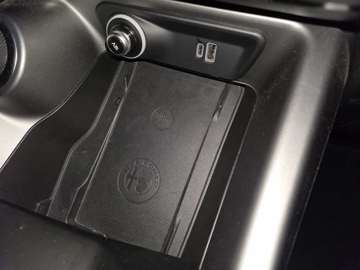 Gros plan sur la console centrale noire de l'Alfa Romeo Tonale 2023 avec zone de recharge sans fil et ports USB.