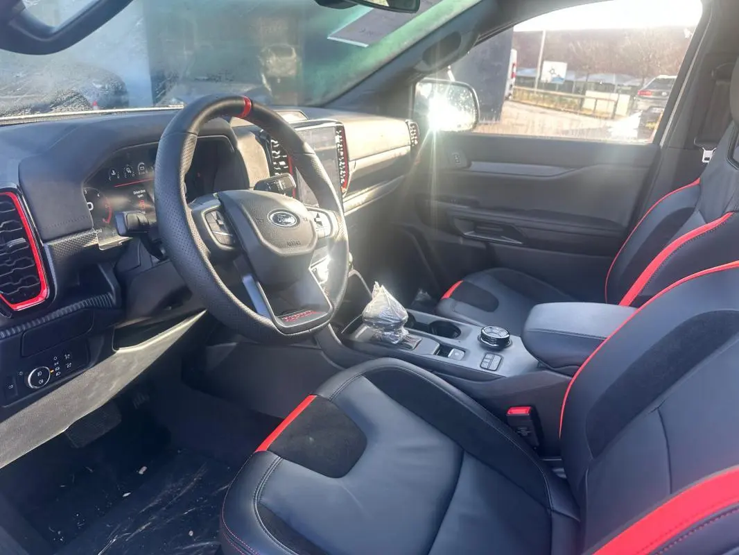 Vue intérieure côté conducteur du Ford Ranger Raptor 2025, sièges noirs avec surpiqûres rouges et tableau de bord moderne.