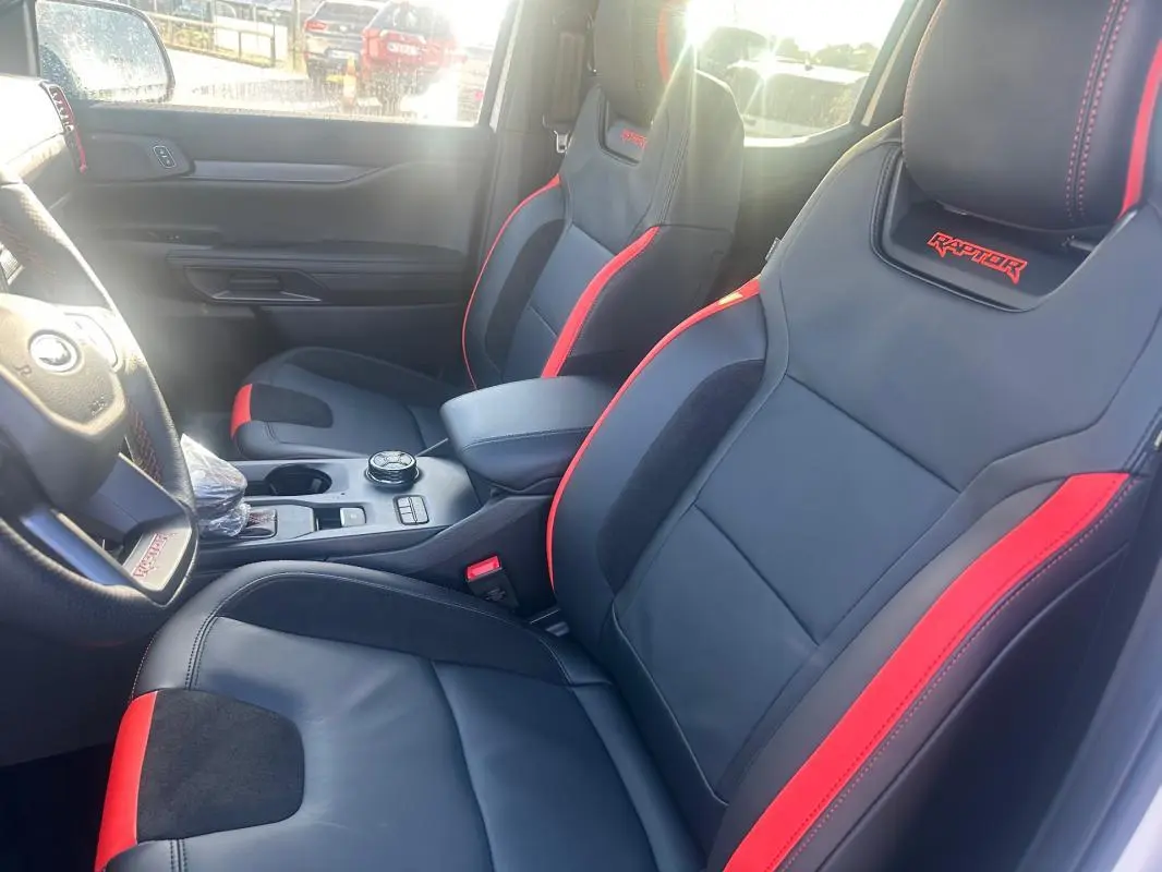 Vue intérieure côté conducteur du Ford Ranger Raptor 2025, sièges noirs avec surpiqûres rouges et logo Raptor brodé.