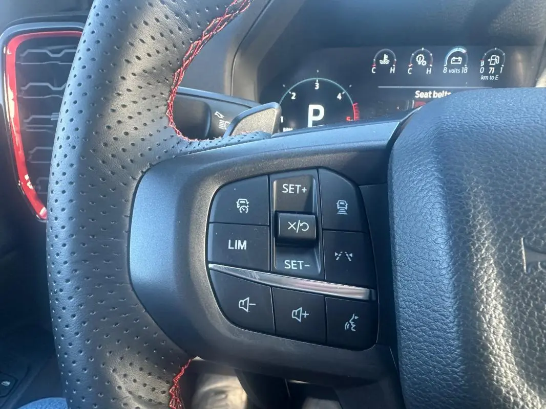 Gros plan sur le volant noir perforé avec surpiqûres rouges du Ford Ranger 2025, montrant les commandes multifonctions à gauche.