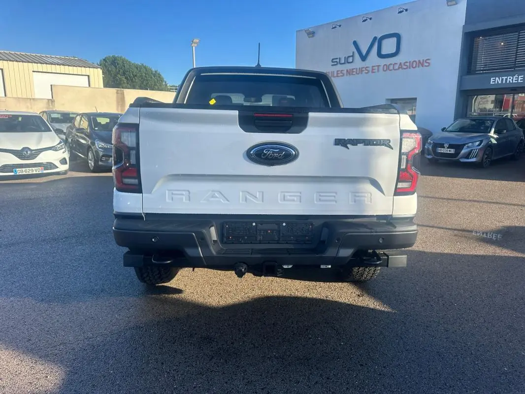 Vue arrière d'un Ford Ranger Raptor blanc 2025 avec logo Ford et inscription RANGER en relief sur la benne.