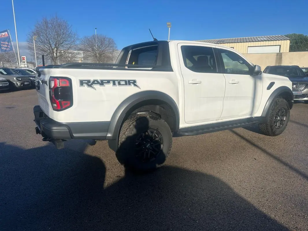 Ford Ranger Raptor blanc vu de trois quarts arrière droit, avec logo "Raptor" et jantes alliage noires.