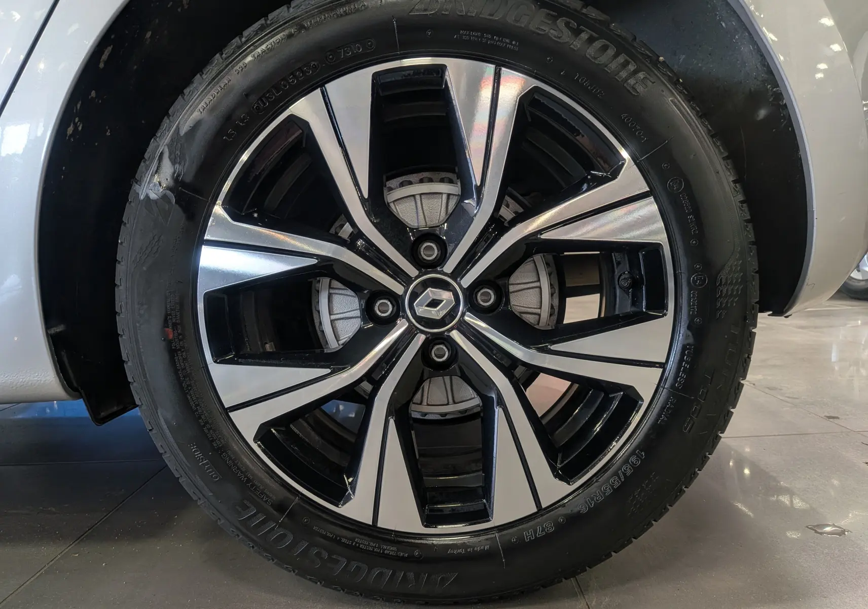 Gros plan sur la jante alliage bicolore noir et argent d'une Renault Clio V gris platine, roue avant droite visible.
