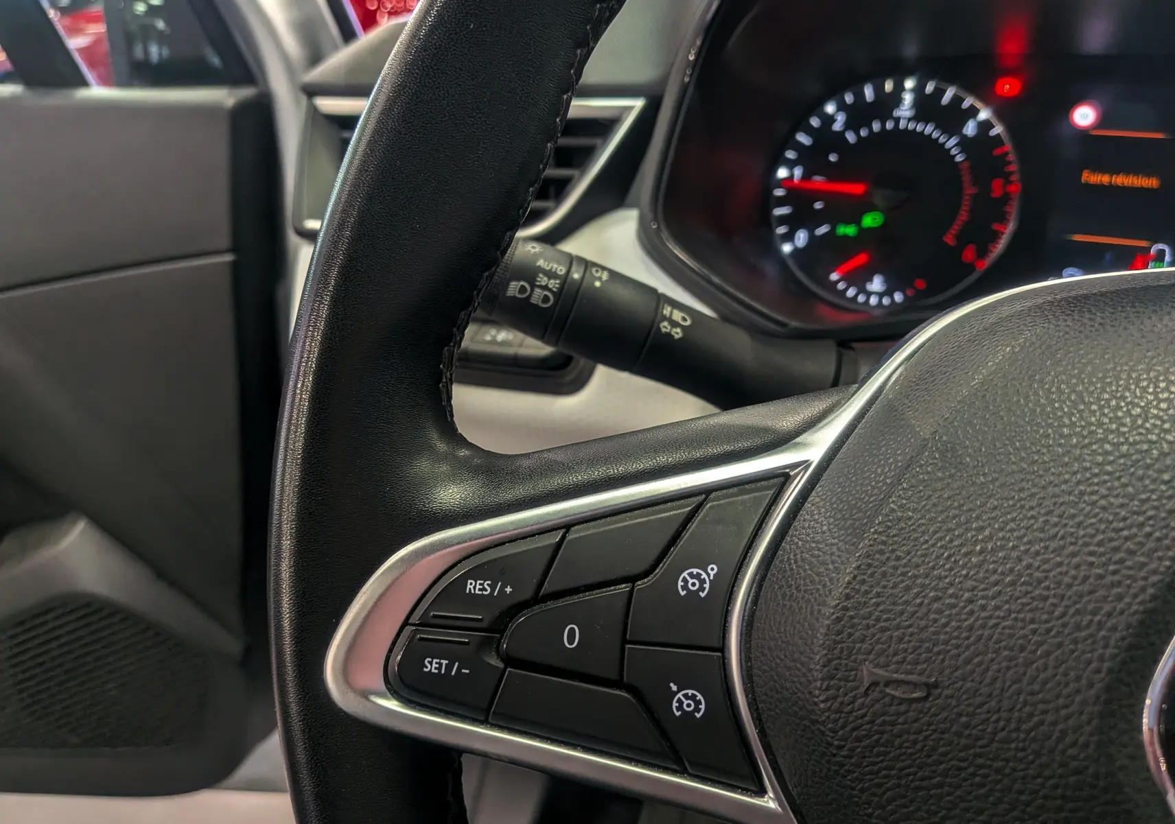 Gros plan sur le volant noir de la Renault Clio V gris platine, montrant les commandes de régulateur de vitesse à gauche.