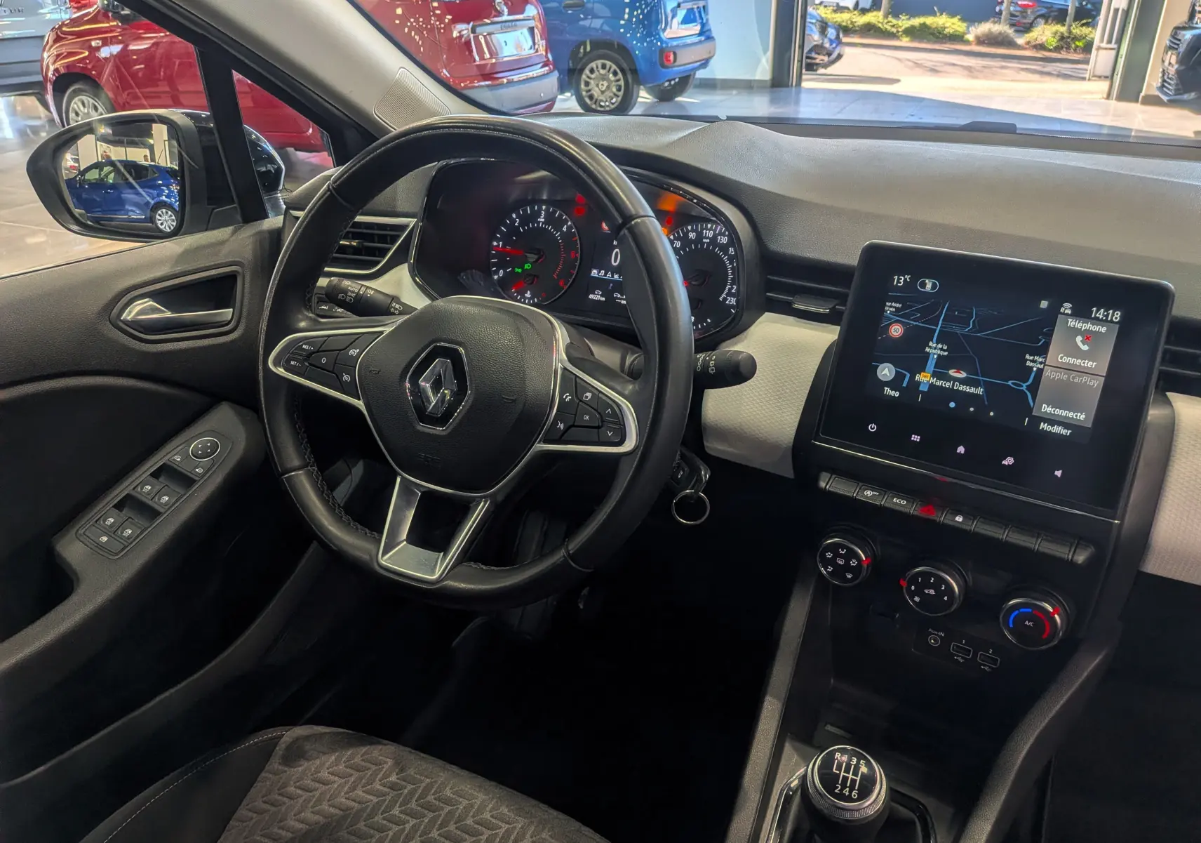 Vue intérieure côté conducteur de la Renault Clio V gris platine, montrant le volant, tableau de bord et écran tactile central.