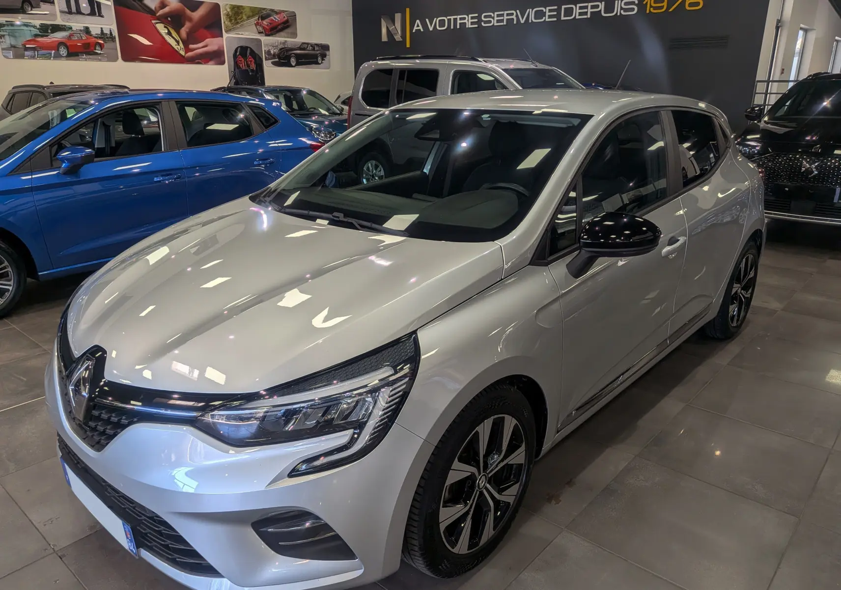 Vue 3/4 avant droite d'une Renault Clio V gris platine en showroom, avec jantes bi-ton et rétroviseurs noirs.