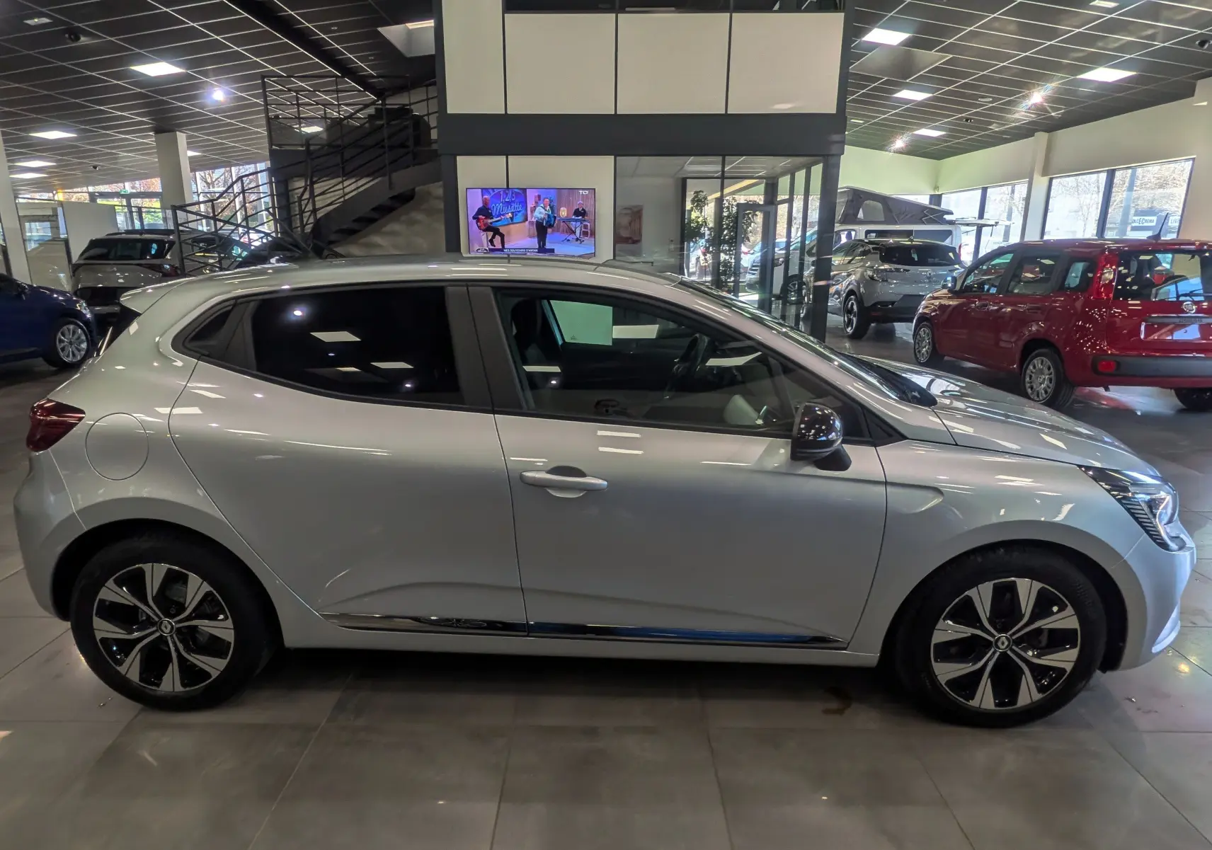Vue de profil côté gauche d'une Renault Clio V gris platine en showroom, avec jantes bi-ton et vitres teintées.