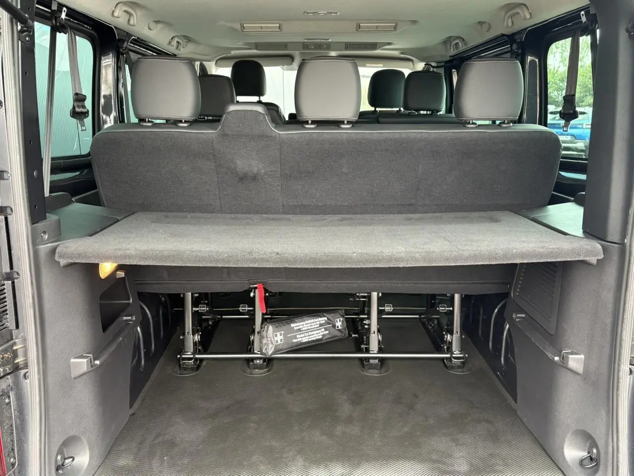 Vue arrière du coffre ouvert du Nissan Primastar gris, montrant la banquette arrière et la tablette de séparation.
