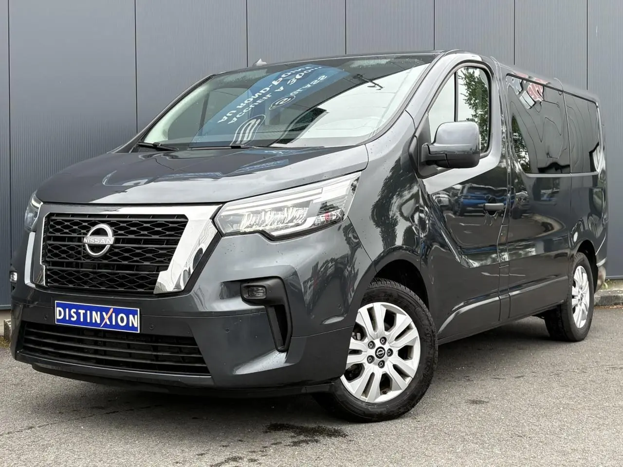 Nissan Primastar gris Comète en 3/4 avant droit, avec hayon vitré et jantes alliage 17 pouces visibles.