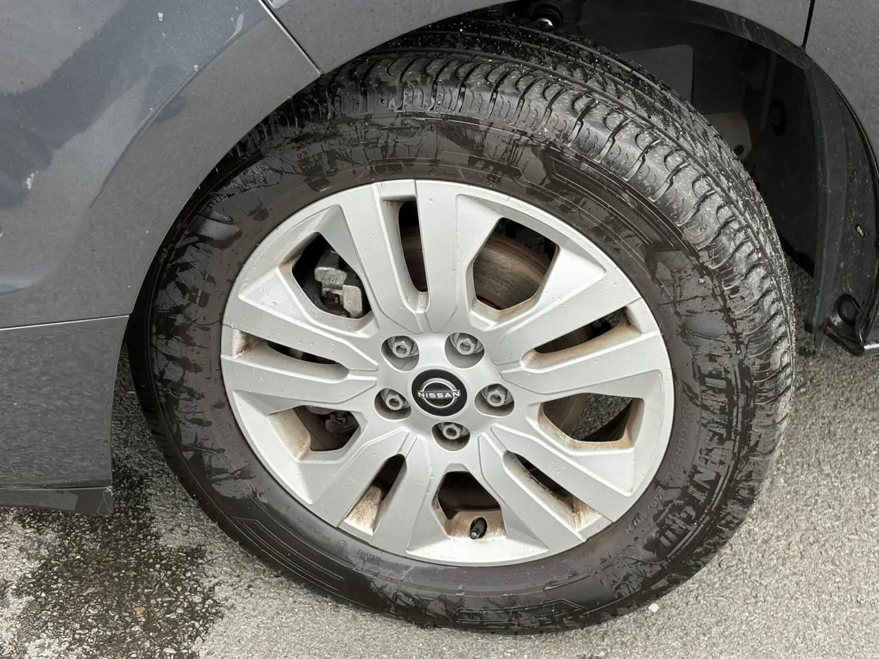 Gros plan sur la jante alliage 17 pouces grise d’un Nissan Primastar gris Comète, avec pneu humide et logo central Nissan.