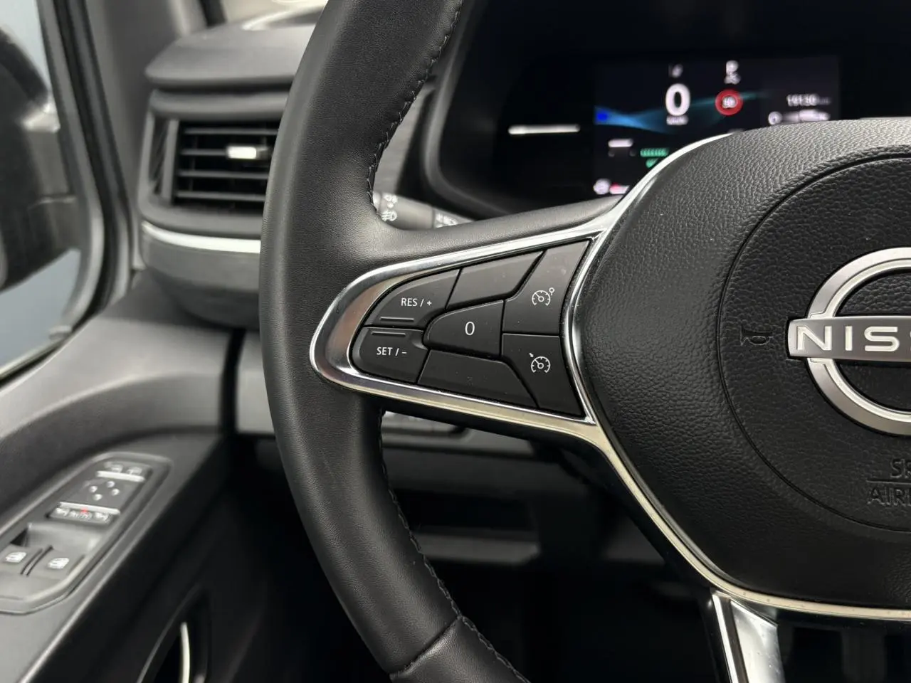 Vue rapprochée du volant noir du Nissan Primastar 2025 avec commandes au volant et tableau de bord numérique en arrière-plan.