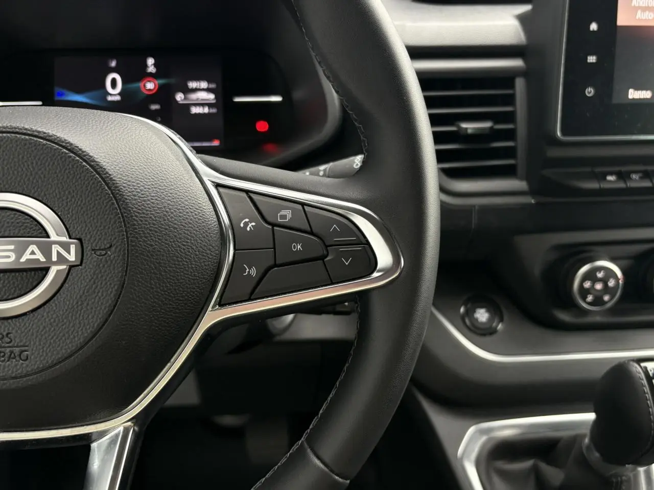 Vue rapprochée du volant noir et du tableau de bord du Nissan Primastar gris Comète avec commandes au volant et écran multifonction.