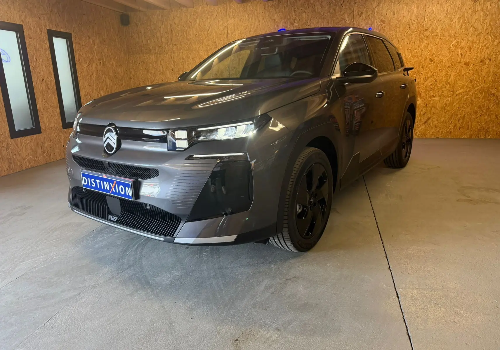 Vue 3/4 avant droite d'un Citroën C5 Aircross gris 2026 avec calandre moderne et jantes noires dans un garage.