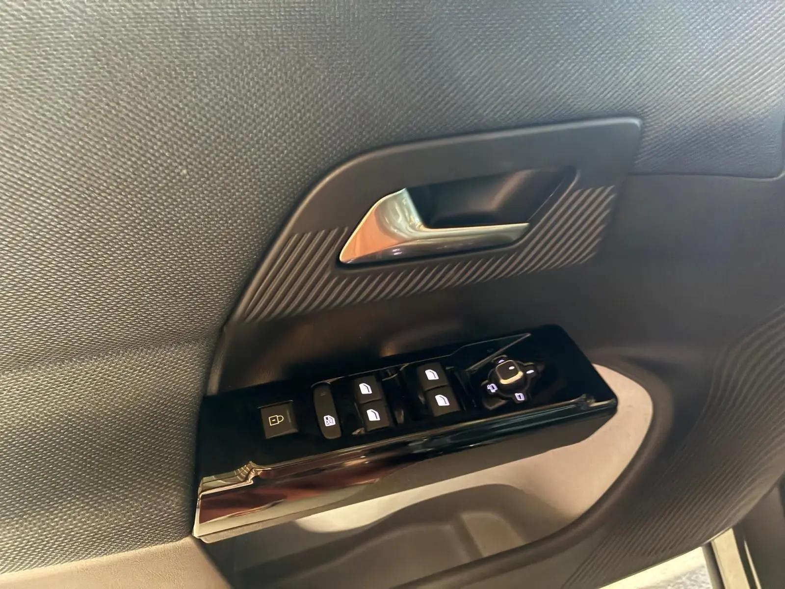 Gros plan sur la commande des vitres et la poignée intérieure côté conducteur d’un Citroën C5 Aircross gris, finition 2026.