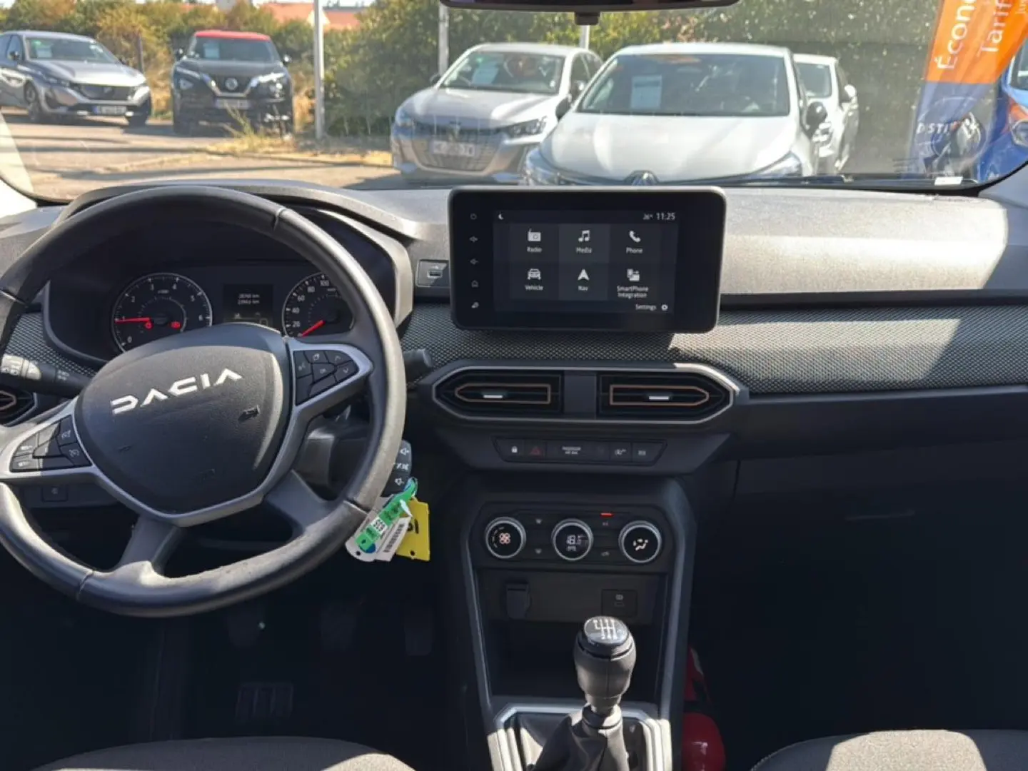 Vue intérieure avant du tableau de bord et volant de la Dacia Sandero 2025, avec écran tactile et levier de vitesse manuel.