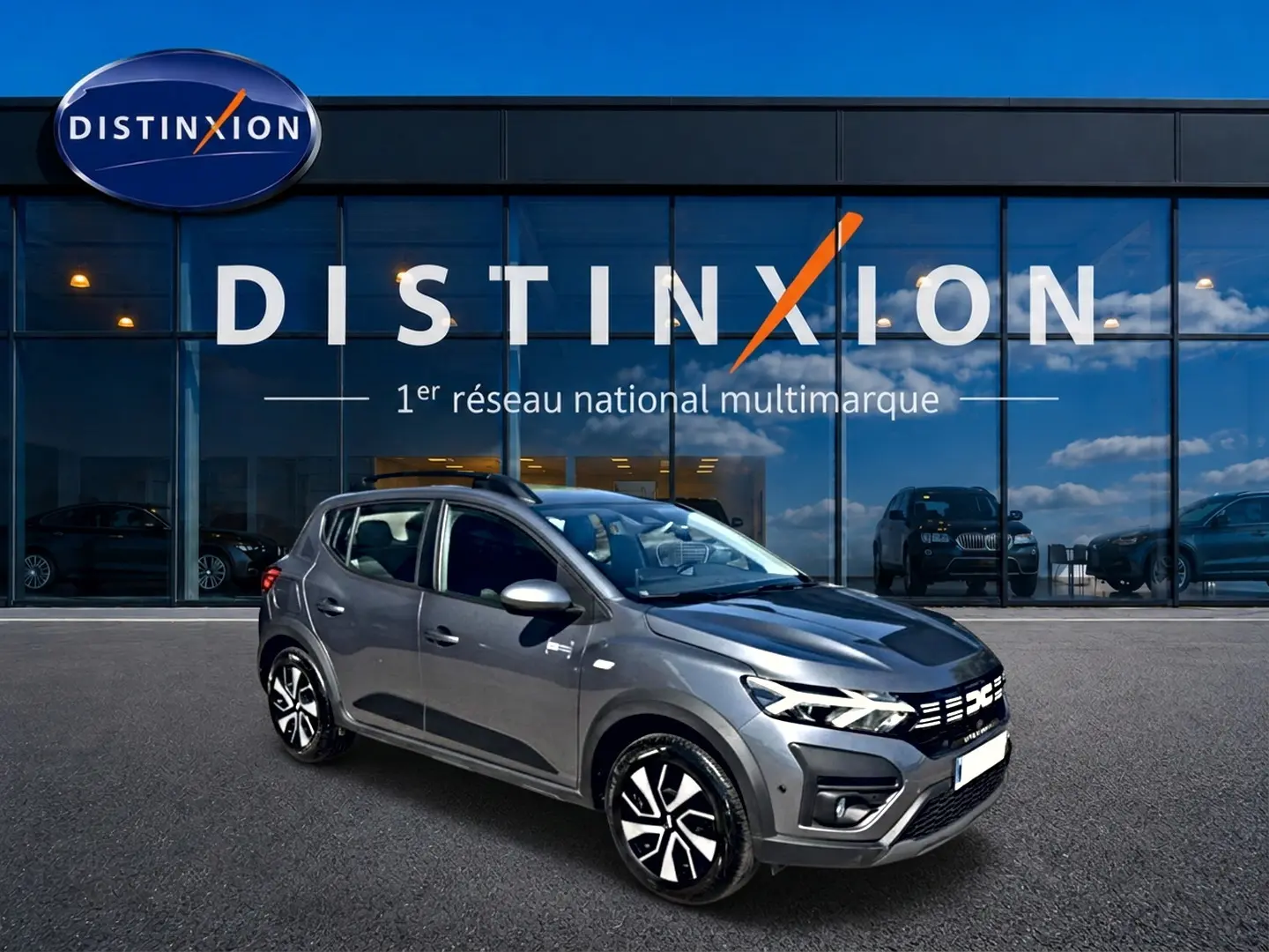Vue 3/4 avant droit d'une Dacia Sandero Stepway gris schiste avec barres de toit et jantes distinctives.