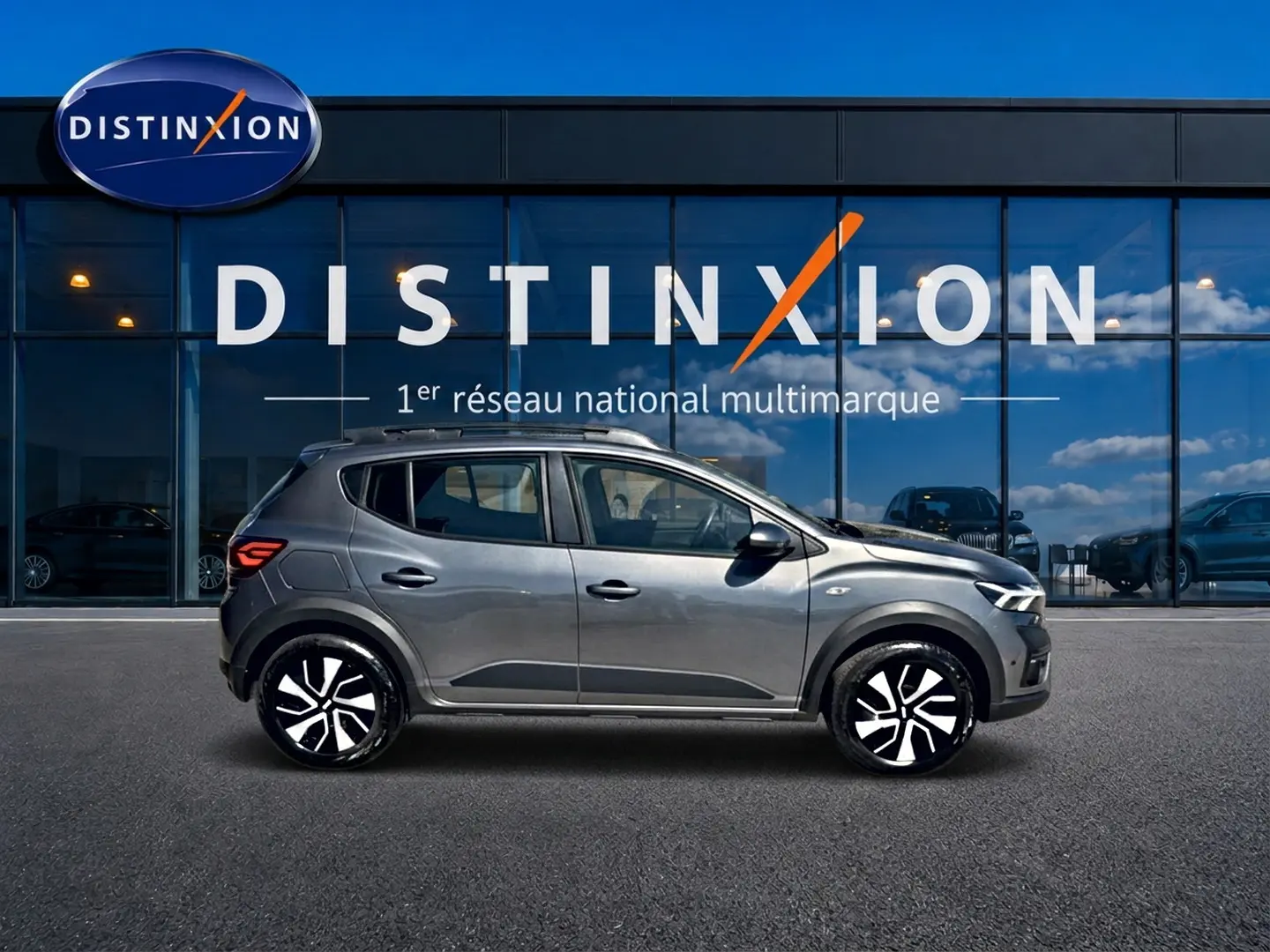 Vue de profil côté gauche d'une Dacia Sandero Stepway 2025 gris schiste avec barres de toit et jantes distinctives.