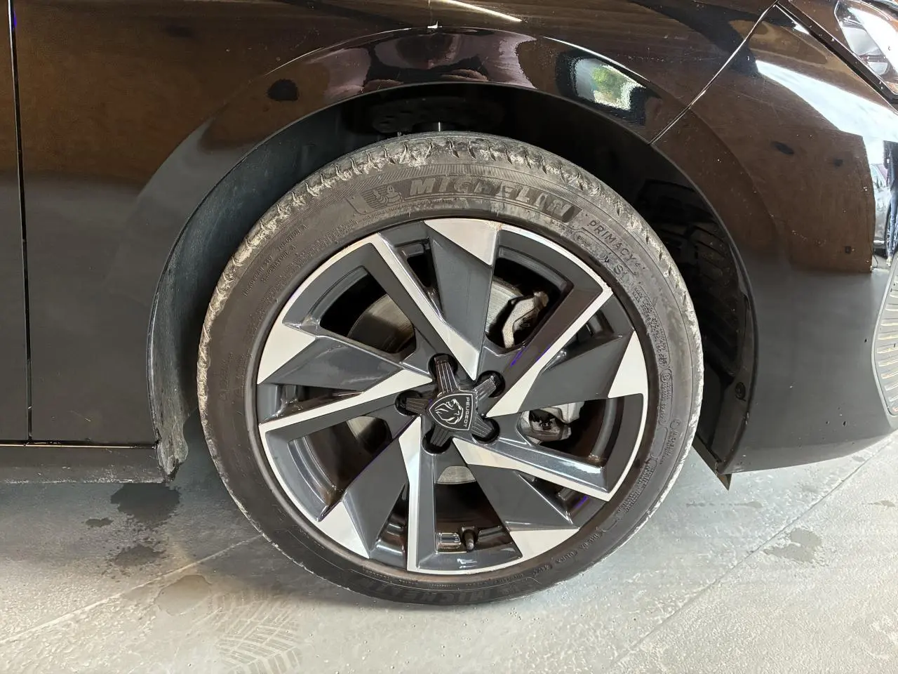 Gros plan sur la roue avant gauche de la Peugeot 308 SW noire, jante alliage 17'' Halong diamantée avec logo Peugeot central.