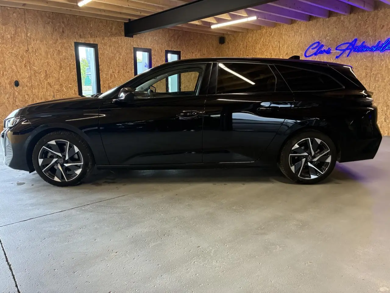 Peugeot 308 SW noire vue de profil droit dans un garage avec jantes alliage et vitres surteintées.