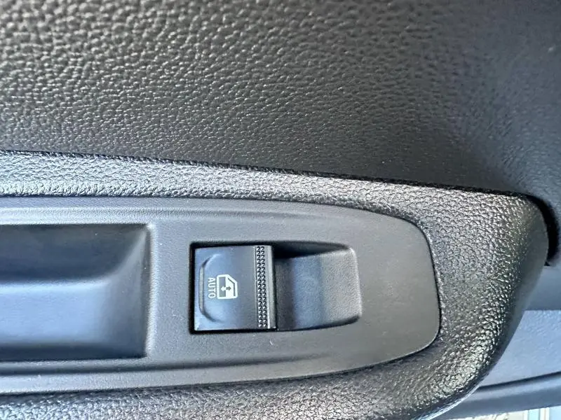 Gros plan sur le bouton de commande de vitre électrique côté conducteur de la Renault Clio gris Rafale.