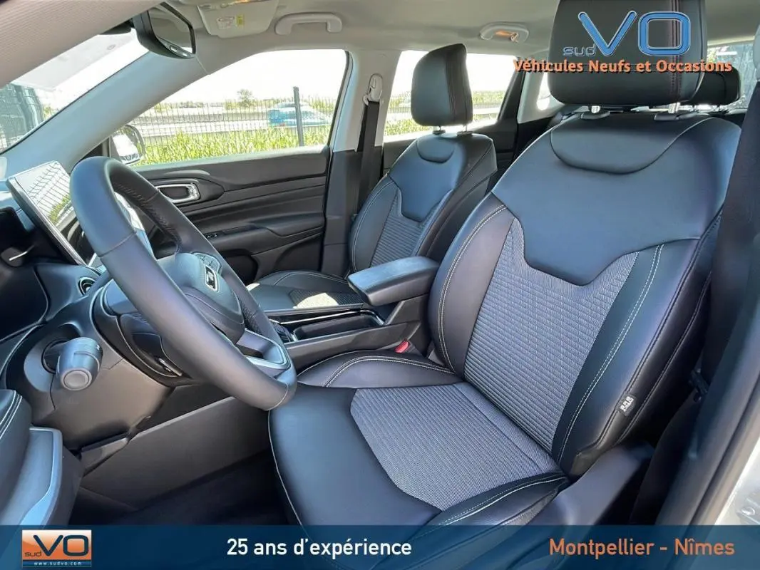 Vue intérieure côté conducteur du Jeep Compass 2024 blanc, sièges noirs en cuir avec accoudoir central et volant multifonction.